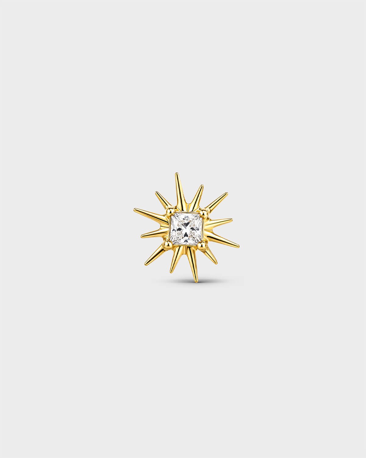 Gold titanium threadless end with a princess-cut clear stone set within a sculpted starburst design. On a light grey background.