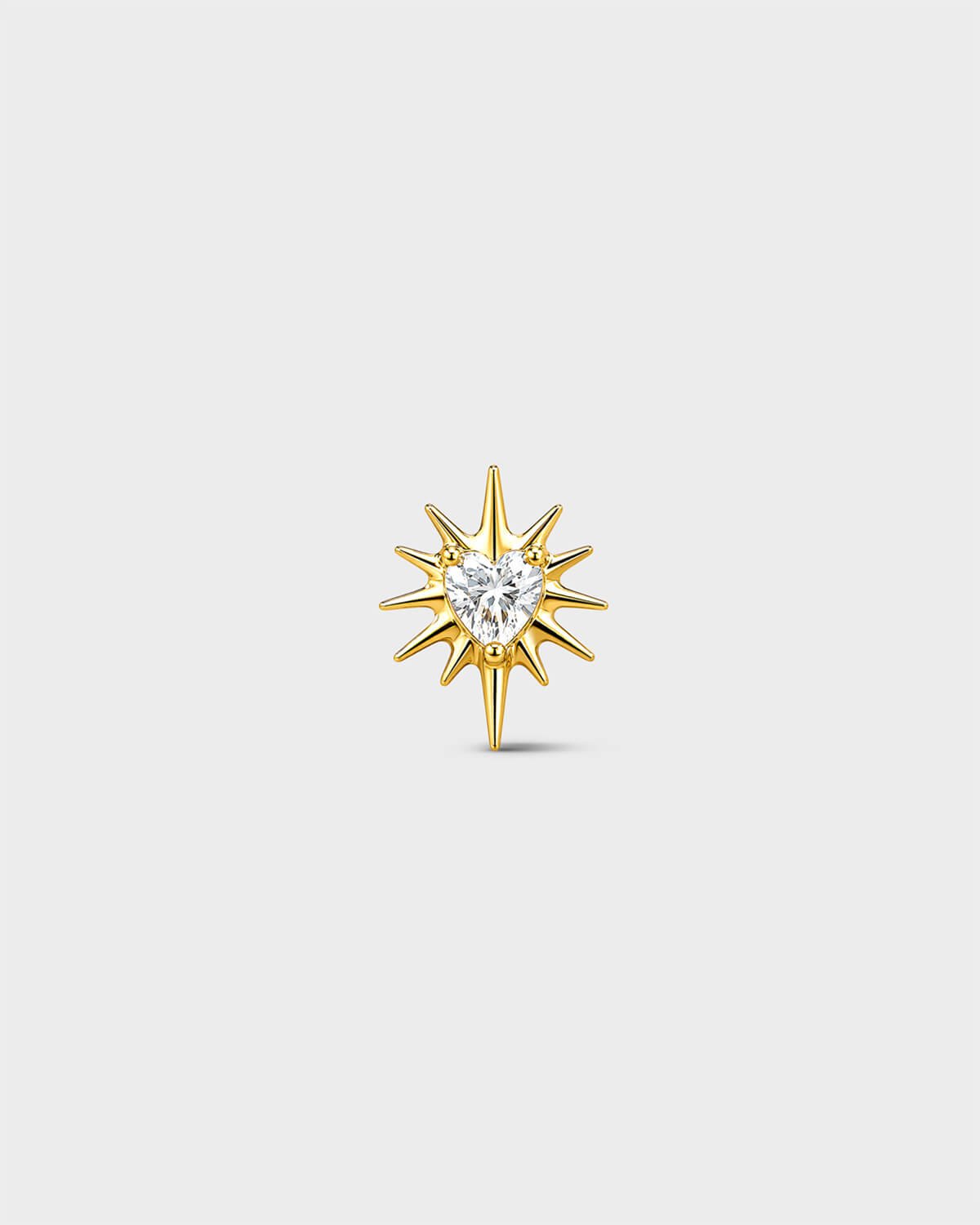 Gold titanium threadless end earring with a heart-cut clear stone set within a sculpted starburst design. On a light grey background.
