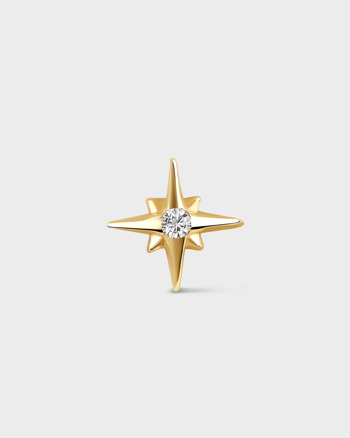 Yellow gold star shape earring with central clear gemstone on a light gray backround