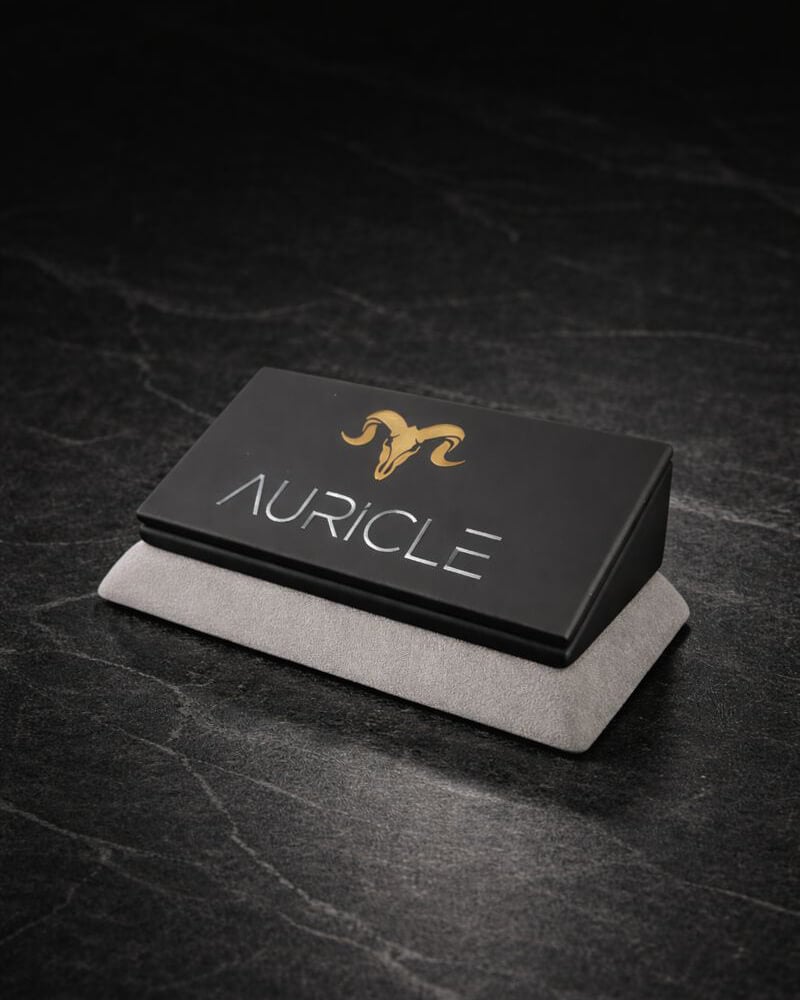 AURICLE jewellery branded nameplate stand. The stand has a light gray suede base with a black leather top. Sat on a dark worktop with moody lighting.