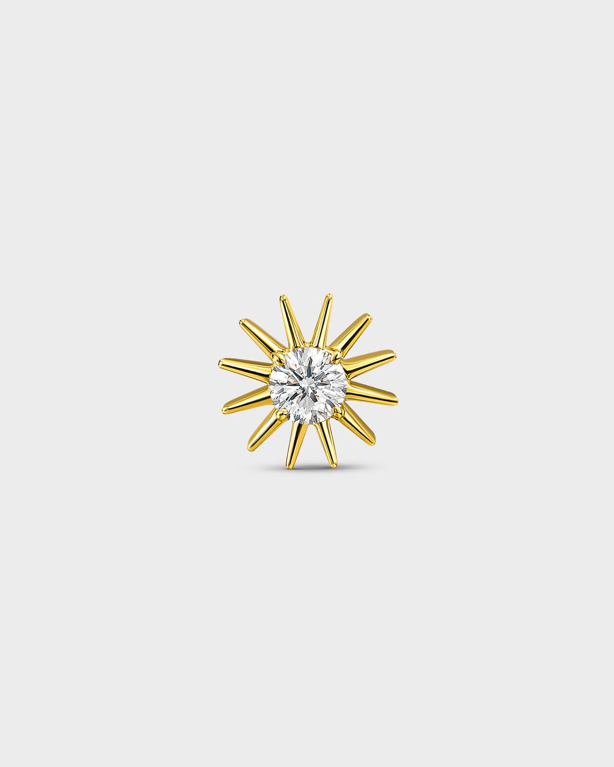 Gold titanium threadless end earring with a round-cut clear stone set within a sculpted starburst design. On a light grey background.